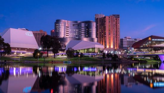 Image of Adelaide skyline, building illuminated at night along the River Torrens.