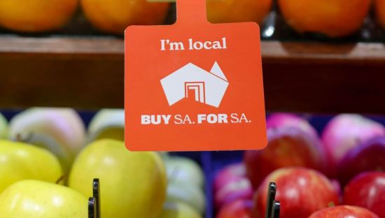 Image of BUY SA logo on a red card attached to a produce display at a greengrocer.