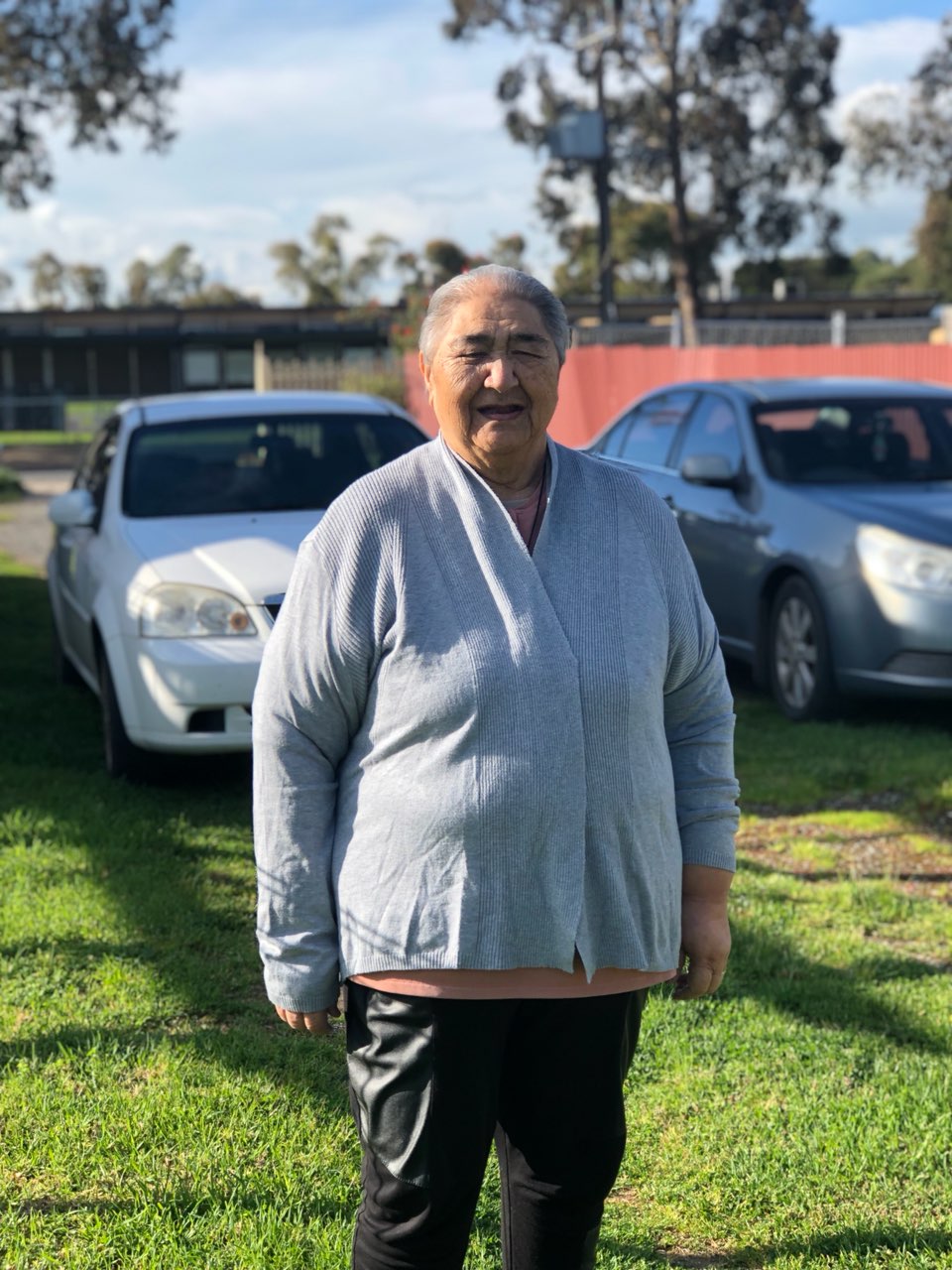 Image of Myra Langdon, standing in front of cars. She is wearing a grey cardigan.