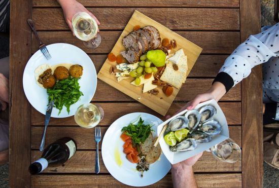 Image of platters of gourmet food taken from above, including oysters, cheese platter, and glasses of wine.