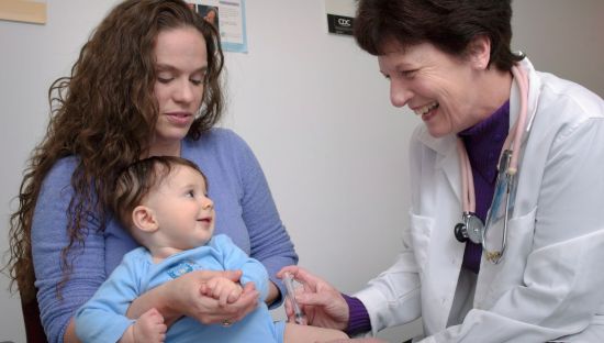 Image of  paediatrician giving a baby a vaccine injection, the baby is held by a woman.