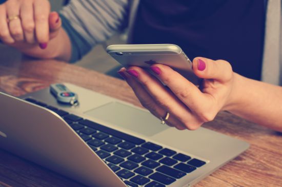 Image of a women at her laptop, also using her mobile phone.