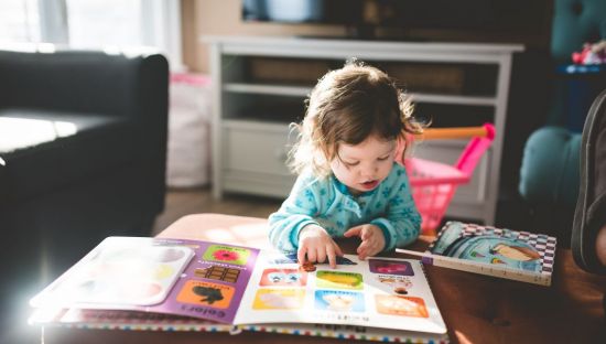 Image of a young child, around one year old, reading books on a coffee table.