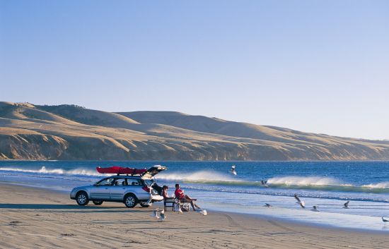 Two people sitting on deck chairs in front of their car on the beach in South Australia 