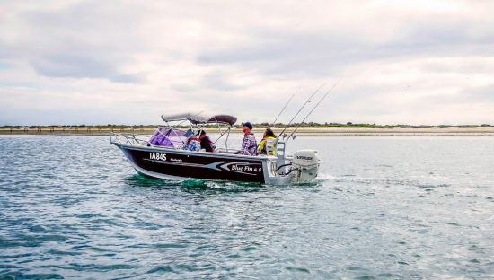 Image of a small fishing boat on the water with 4 people inside with fishing rods.