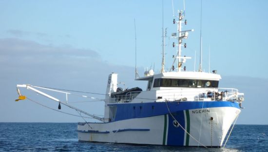 Image of the marine research vessel 'The Ngerin', which is a white boat boat with blue markings. It has a lot of aerials on top of it, along with large booms.