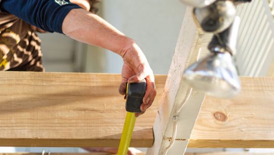 Close up image of a hand measuring wood, on a house build.