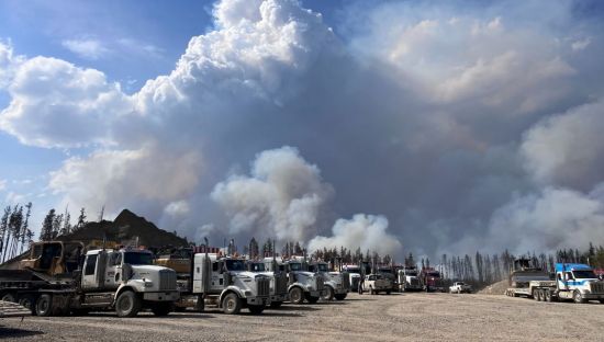 Image of trucks lined up with smoke in the background, they are in Canada. The smoke is from wildfires.