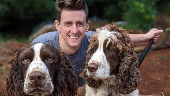Young male pictured smiling with two dogs in foreground.