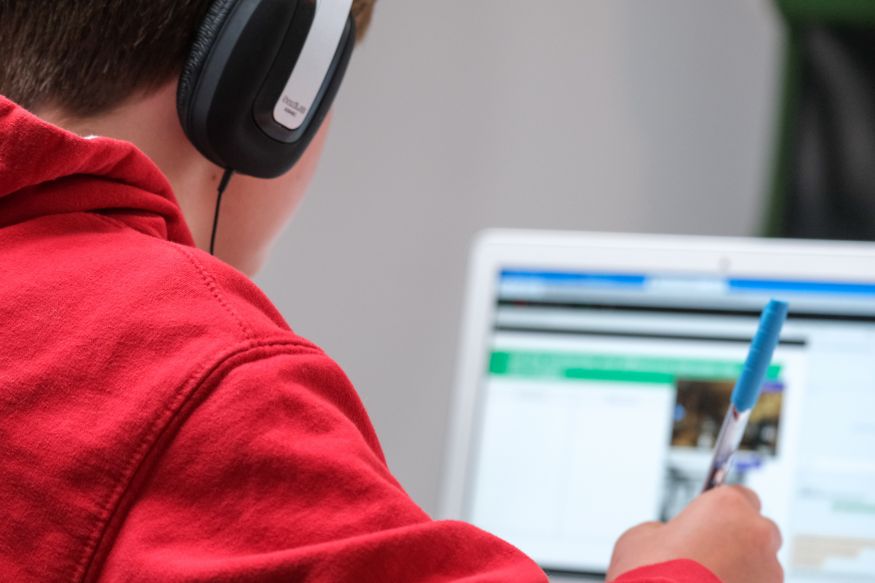 Image of a boy in a red jumper and headphones using a computer for schoolwork.