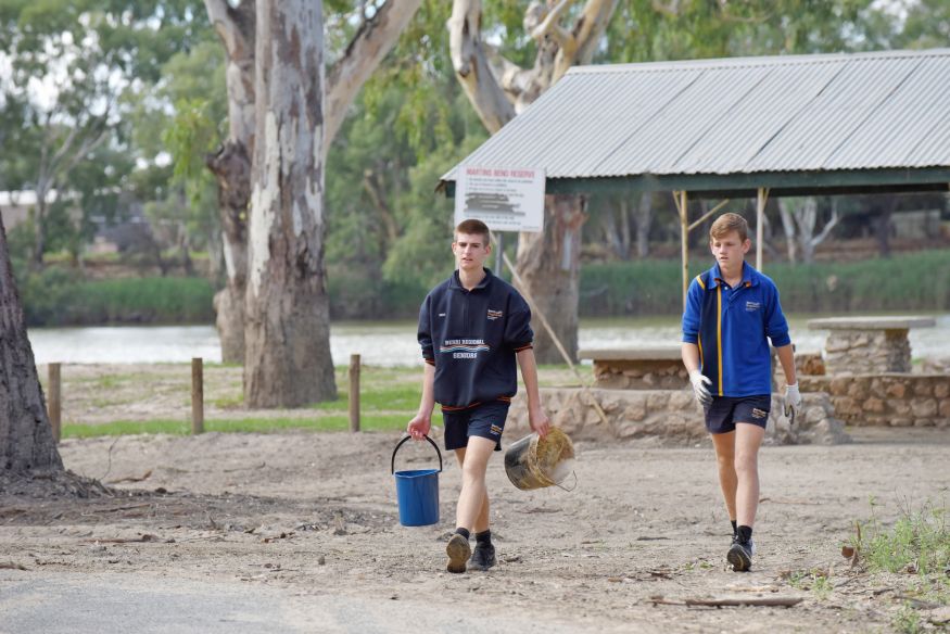 Image of Berri Regional Secondary College students Cameron and Harry moving buckets, they are standing on a riverbank