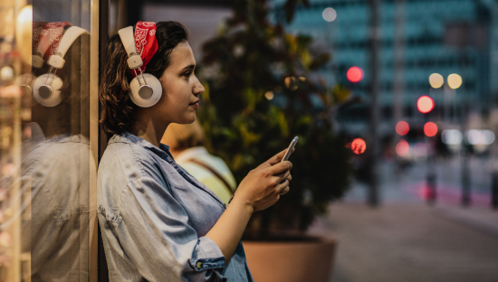 Image of a woman listening to something on her phone whilst wearing headphones.