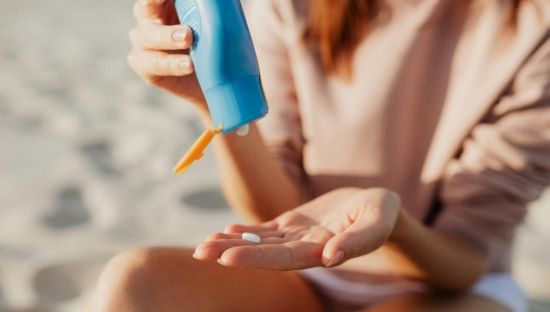 image of woman sitting on beach squeezing sunscreen onto hand from a tube